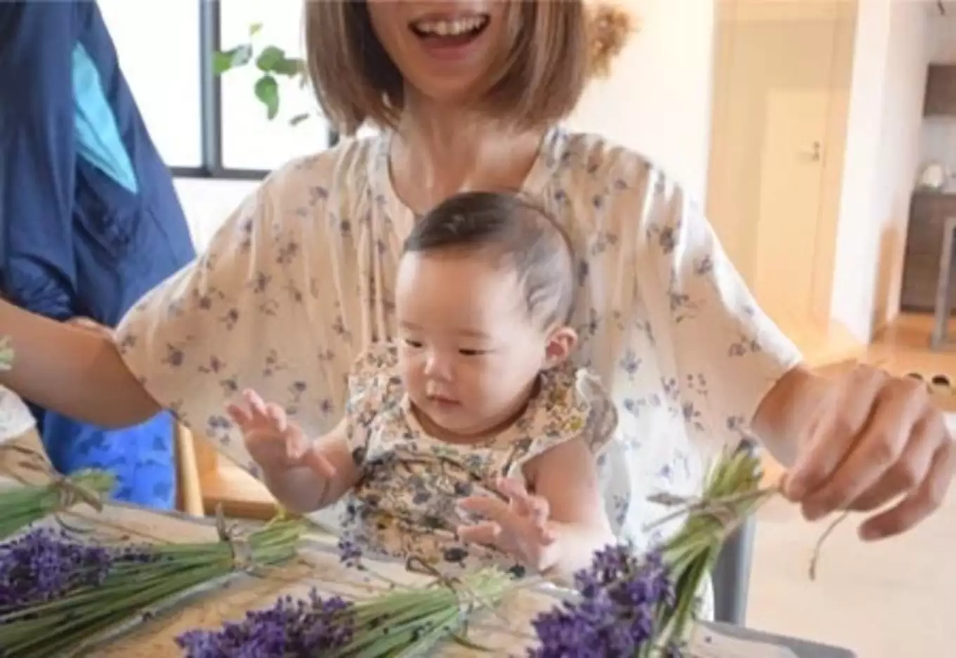 ママのお膝の上でスワッグ作りの応援をする幼児。共にラベンダーのような小花のお洋服で素敵です。