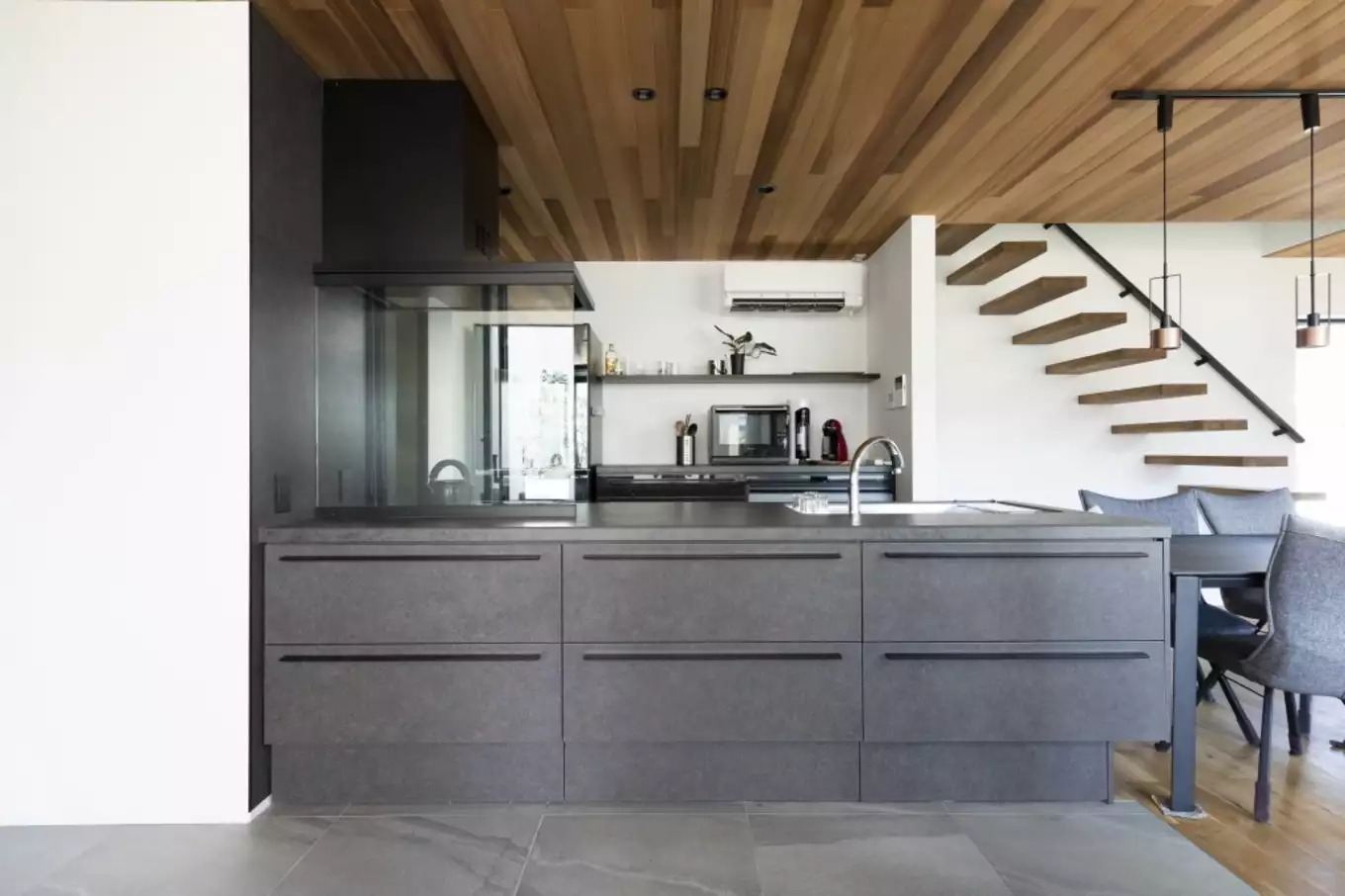 モノトーンのスタイリッシュなキッチンに天井と階段の木目が映えるダイニングキッチン