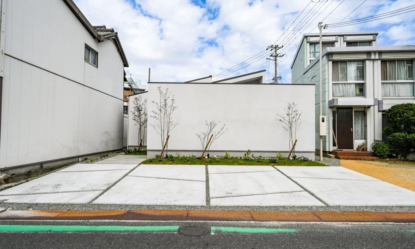 白い外壁とコンクリートの駐車場があるシンプルな外観