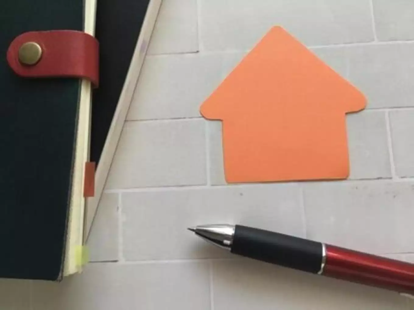 手帳とペンと家の形をしたオレンジ色の紙