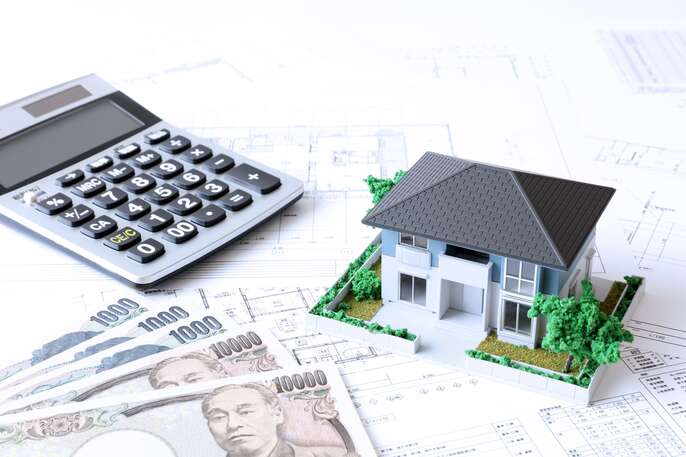 住宅設計図の上に載っている住宅模型と電卓とお金