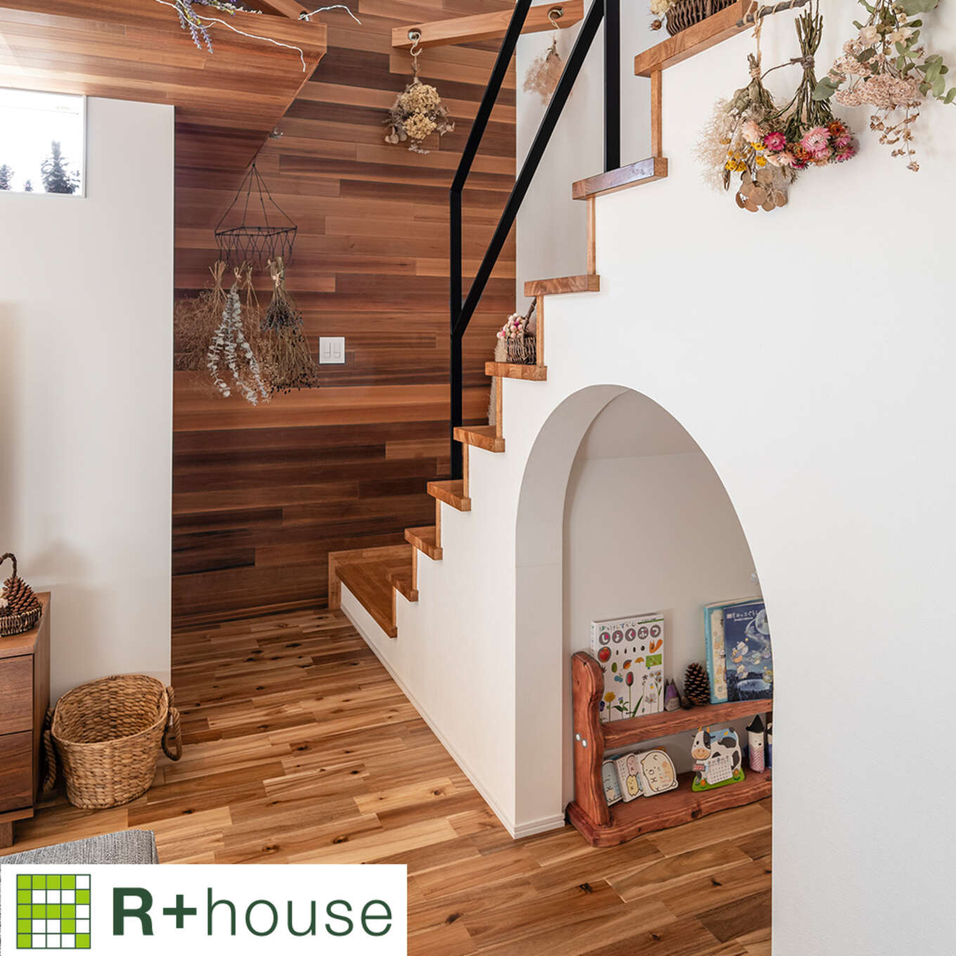 R+houseの物件の階段の写真です。階段下スペースをアーチ型に壁をくりぬき、絵本を置いてある。階段は二階まで吹き抜け。