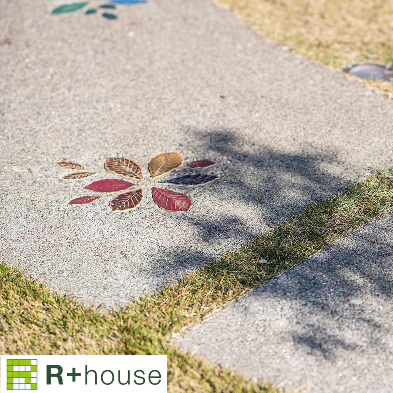 R+houseの物件の庭にある園路の写真です。洗い出し仕上げの園路に赤い葉っぱの形のタイルが花の形に埋め込まれている