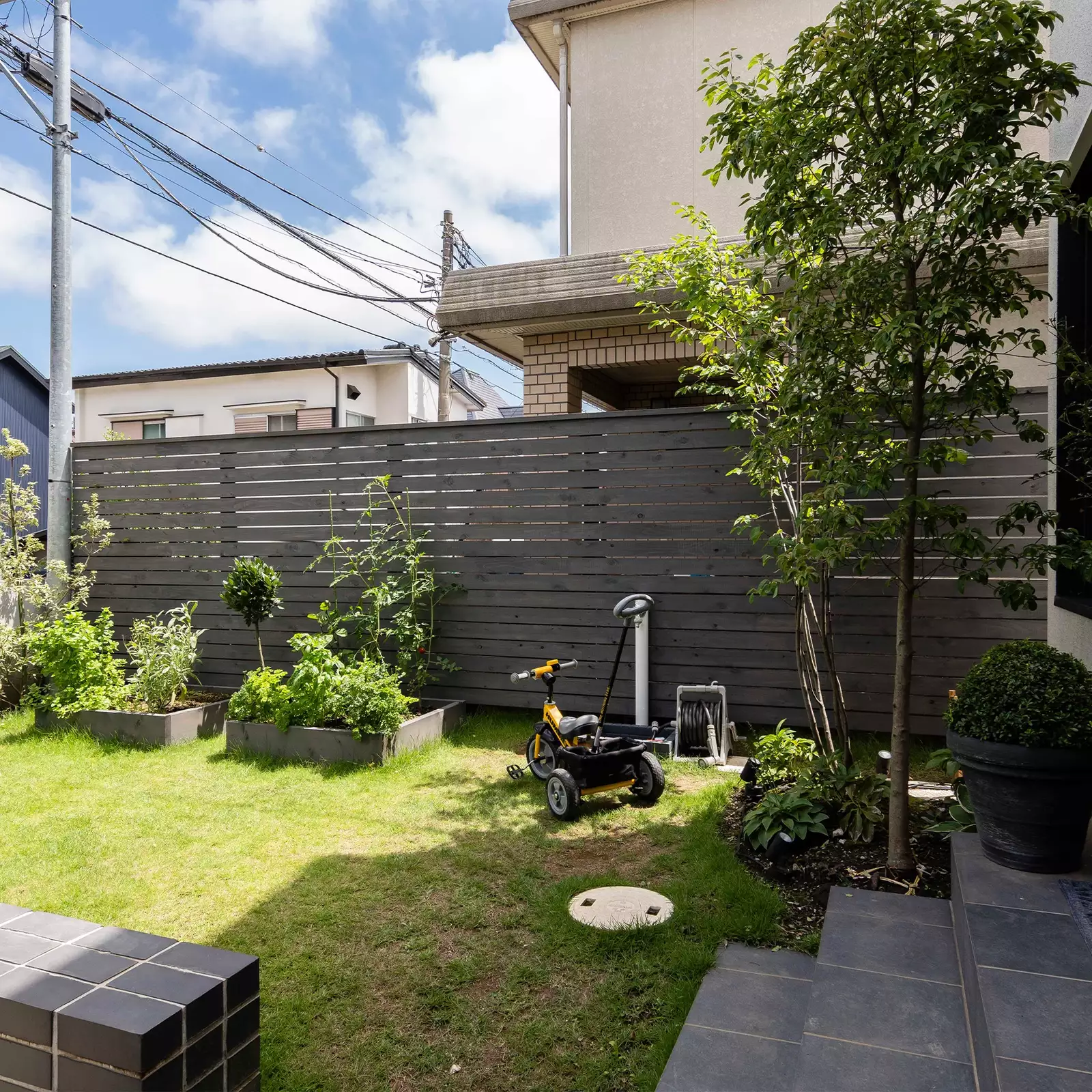R+houseの物件の庭の写真です。木の塀に囲まれた空間に花壇と芝生がある。