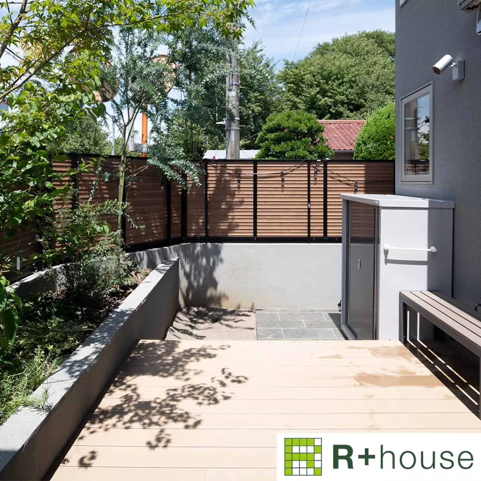 R+houseの物件のウッドデッキの写真です。塀が高く外からは見えないが中からは近隣の緑や空がよく見えるお庭