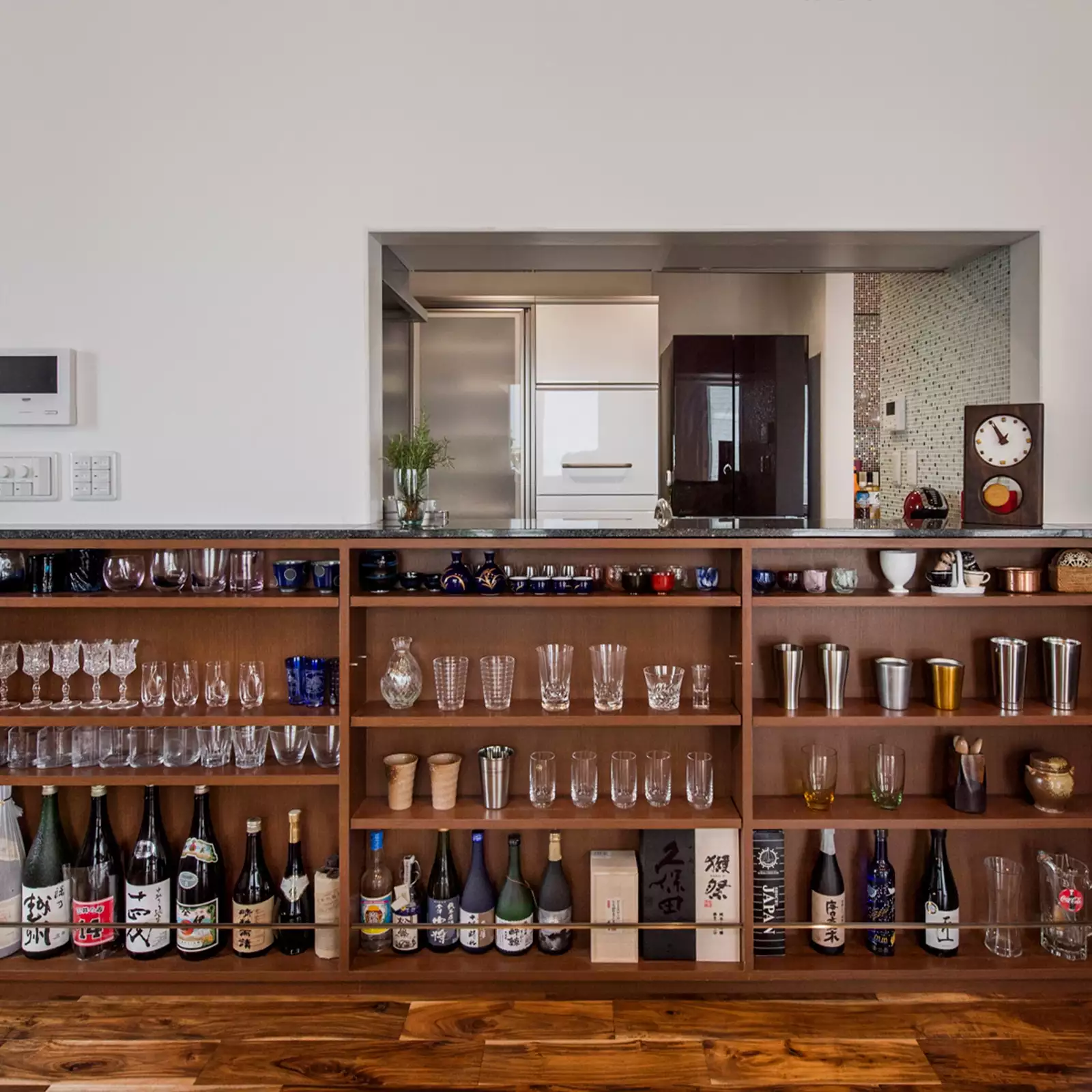 R+houseの物件のオープン棚の写真です。キッチンとつながる窓の下に作られた棚。酒瓶と酒器のコレクションが並ぶ。