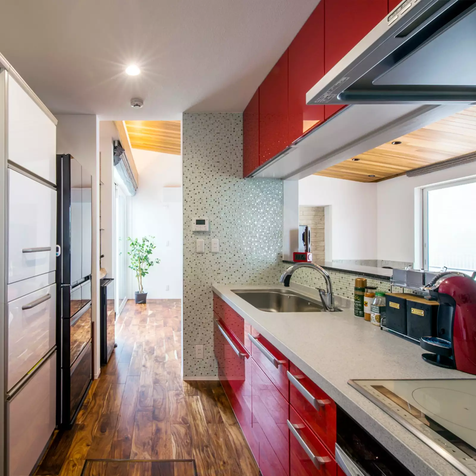 R+houseの物件のキッチンの写真。赤いキッチンが目を引く。流しの向かいはダイニングとつながる窓がある。