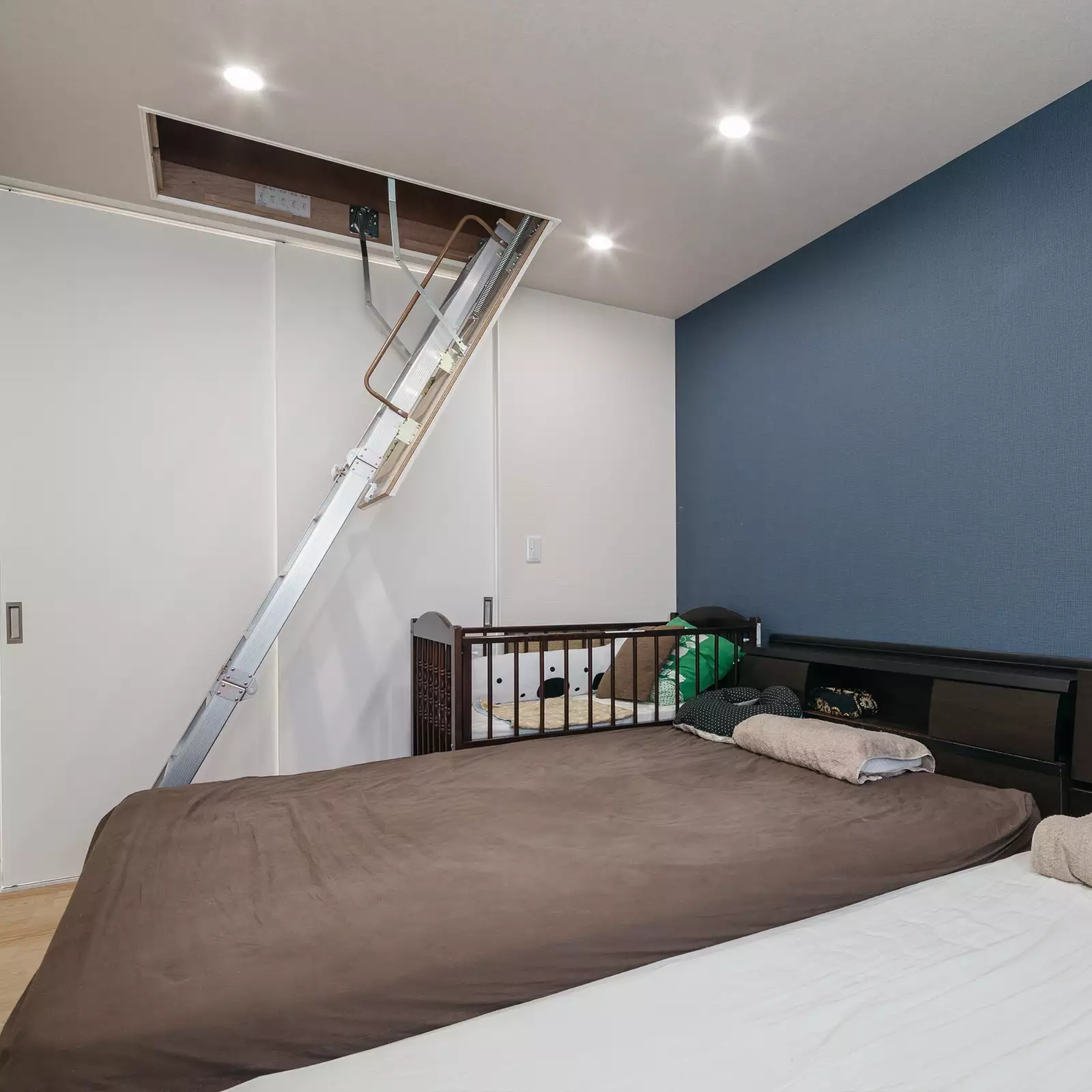 R+houseの物件の寝室の写真です。ベッドがあり、奥には扉。その間の天井から階段が下りており上るとロフトにいける。