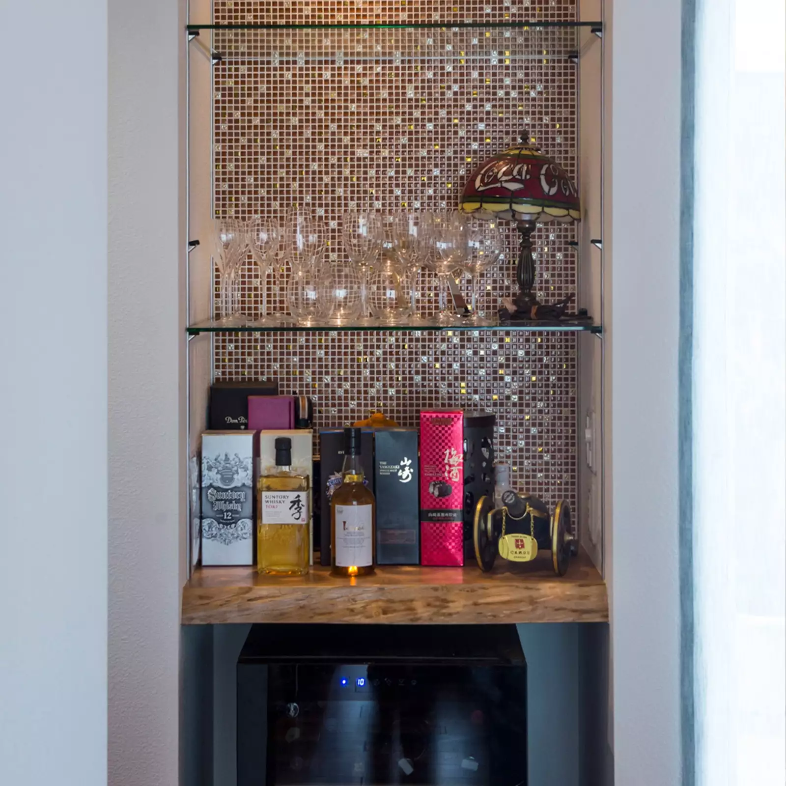 R+houseの物件のバーコーナーの写真です。モザイクタイルを背面に貼った棚にグラスやお酒がある。下部にはワインセラーも。