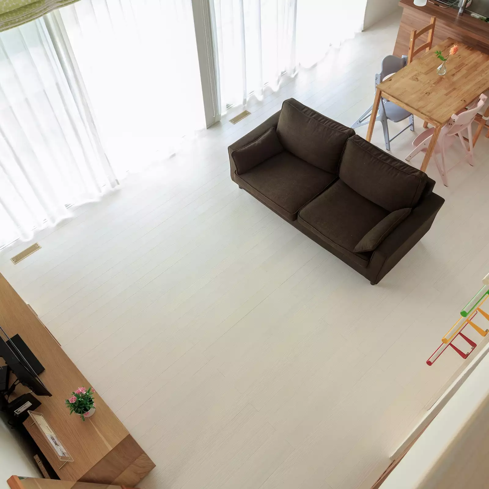 R+houseの物件のＬＤＫをロフトから見た写真です。右からキッチン、ダイニング、ソファーがあり空間をあけてテレビ台がある。