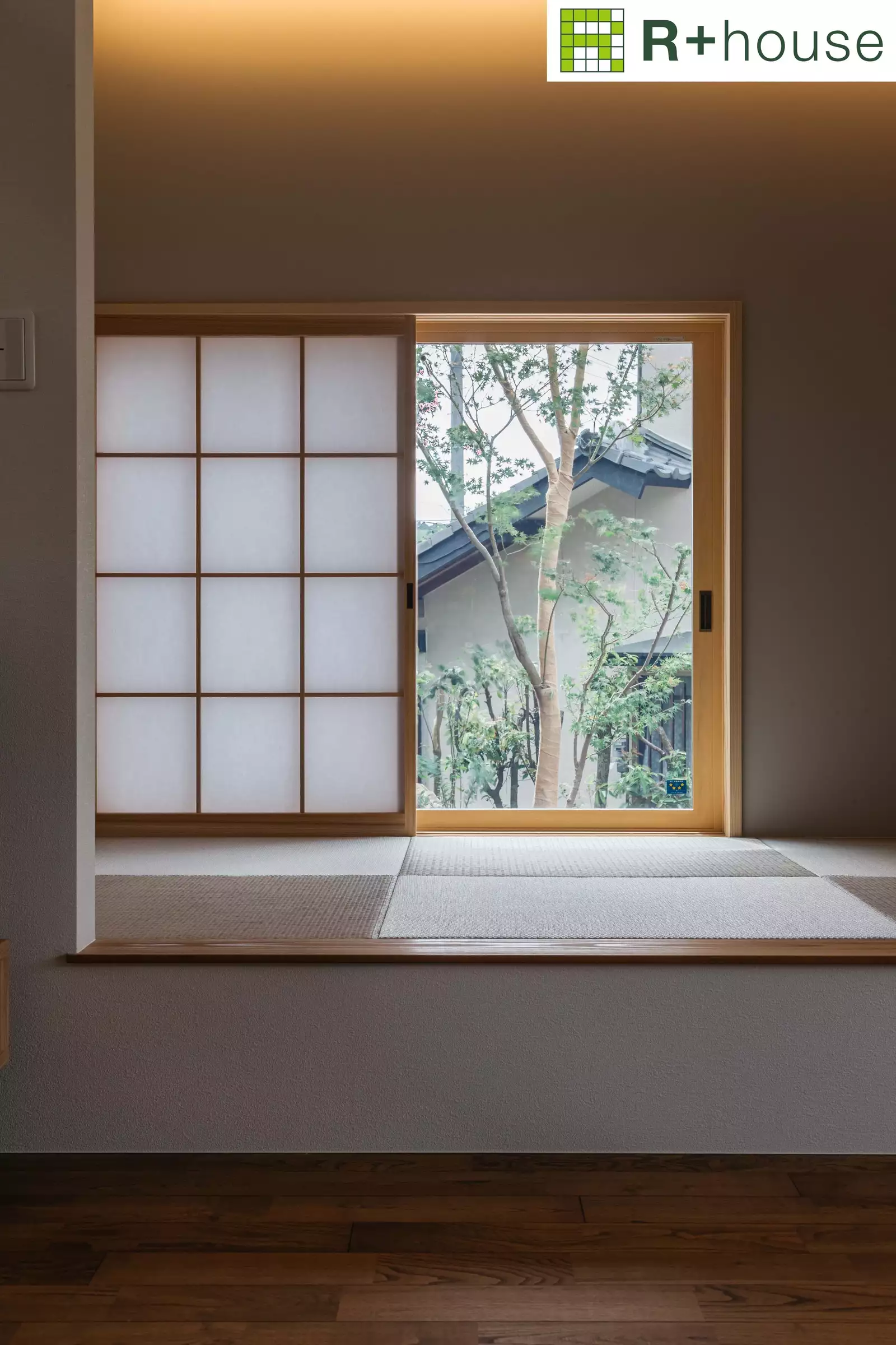 R+houseの物件の和室の写真です。琉球畳に障子と窓、その向こうに木があります。