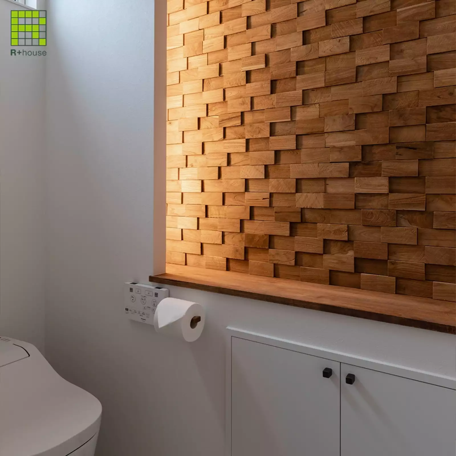 R+houseの物件のトイレの写真です。白を基調としたトイレの壁の一部に天然木をランダムに組み合わせたパネル。