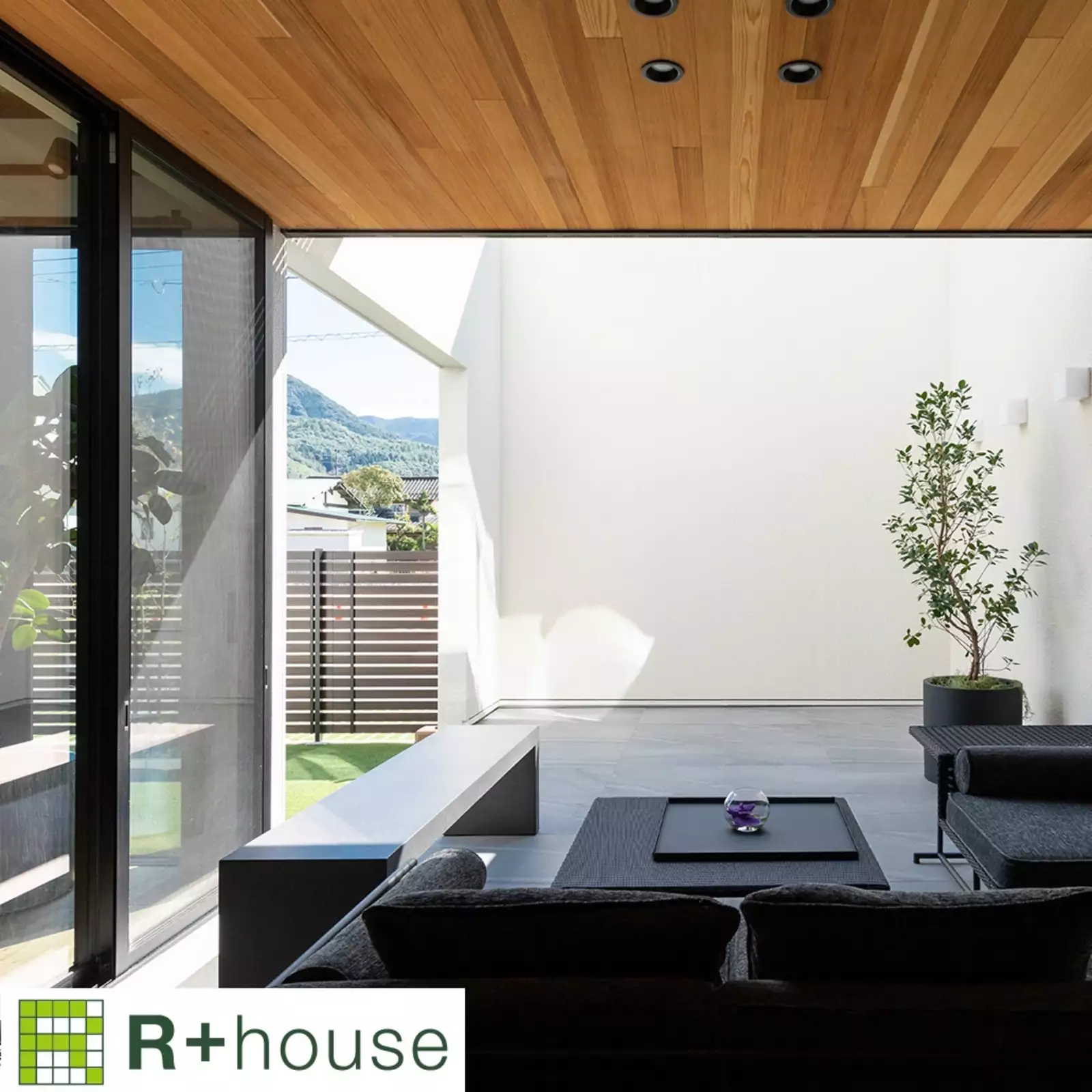 R+houseの物件のテラスの写真です。手前側には屋根があり家具を置き、外側は吹き抜けに。さらに左に出ると芝の庭がある。
