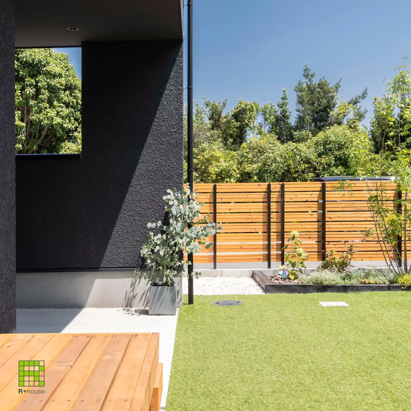 R+houseの物件の庭の写真です。ガレージから抜けてくると芝生の庭が。木でできたデッキと塀がおしゃれ