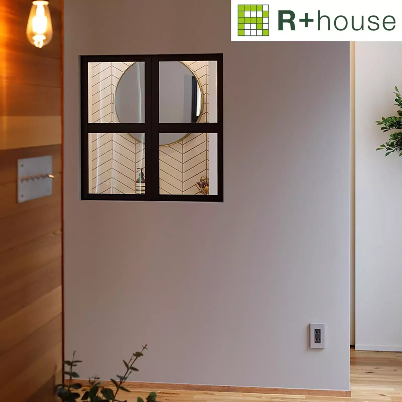 R+houseの物件の玄関からの写真です。玄関の壁はナチュラルな板張り。正面に見える白い壁におしゃれな黒の内窓。内窓から見えるのは洗面の丸鏡。