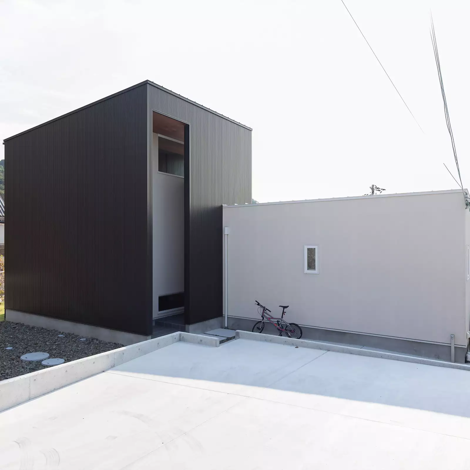 R+houseの物件の外観の写真です。左側は黒いほぼ正方形の建物、右側は少し低い長方形の白い建物がくっついた物件。