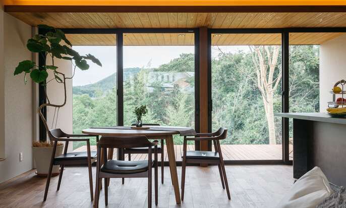 R+houseの物件の内観の写真です。大きな窓からウッドデッキと外の森林が眺められる