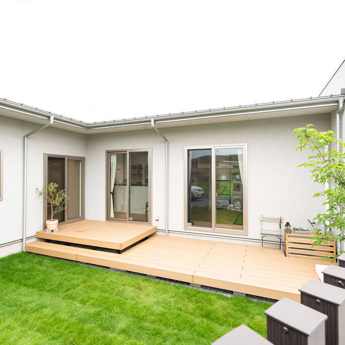 R+houseの物件の写真です。芝生の庭と大きなウッドデッキ、白い平屋の家。