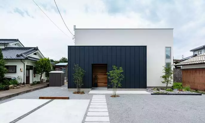 R+houseの住宅の外観写真です。白と黒の建物の前に2台分の駐車スペースとアプローチ、植栽があります。