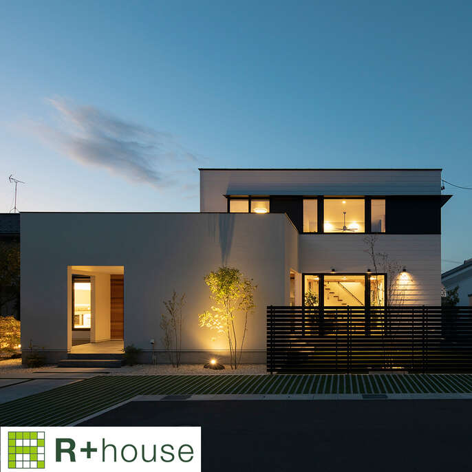 R+houseの物件の写真です。夕暮れの中暖かい光がこぼれる白い二階建てのお家です。