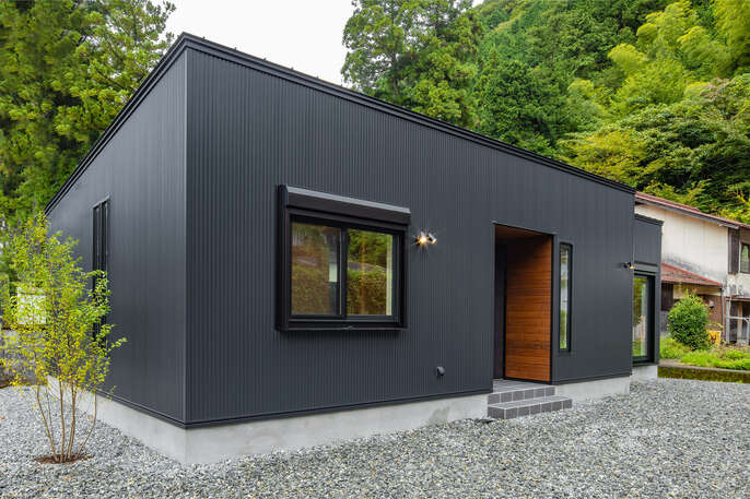R+houseの物件の写真です。豊かな自然の中に黒い外観が目を引く平屋のお家です。