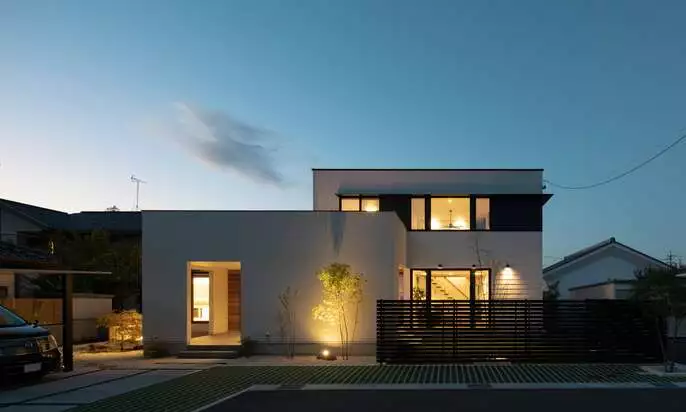 R+houseの物件の写真です。夕暮れの中暖かい光がこぼれる白い二階建てのお家です。