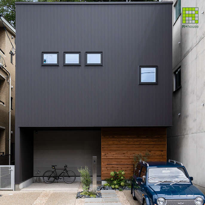 R+houseの物件の写真です。黒い四角い外観がスタイリッシュ。家の前には駐車スペース。窓は小さいのが4っつ