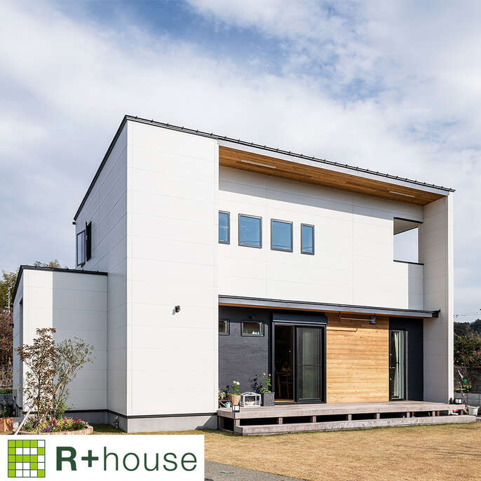 R+houseの物件の写真です。白い壁の二階建てのお家。手前側には広々としたウッドデッキがあります。