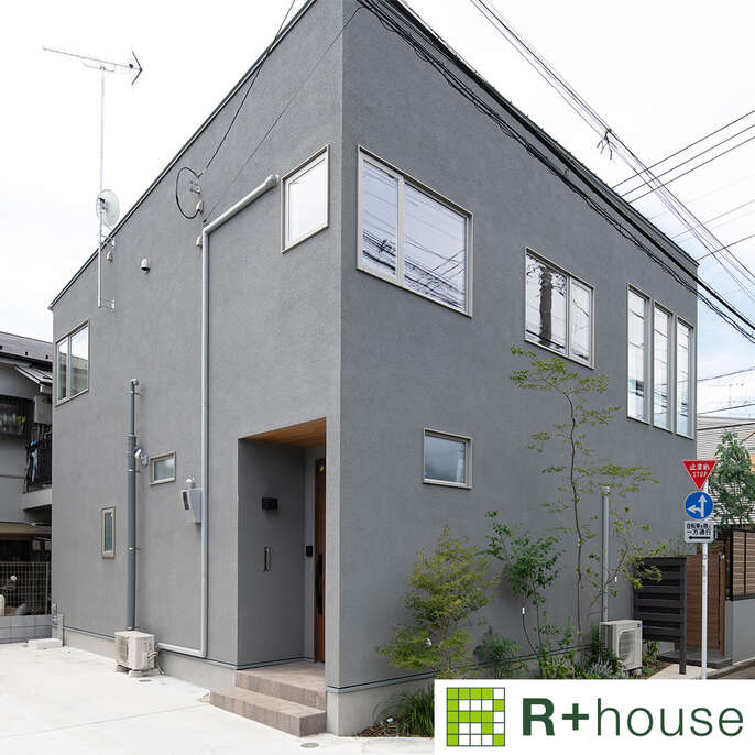 R+houseの物件の写真です。グレーの壁のスタイリッシュな家。道路と家の間に植えた木々が映える。