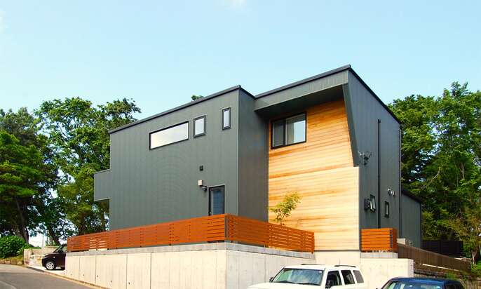 緩やかな斜面に建つモスグリーンの家、一部木板貼りで温かみのある家