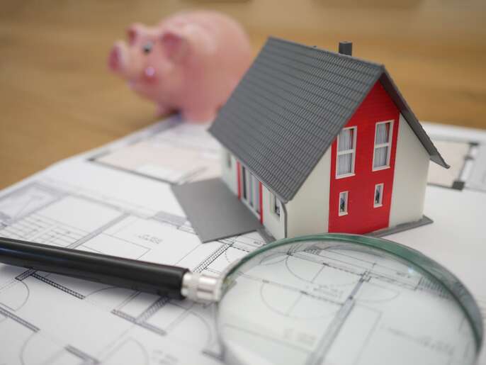 グレーの虫眼鏡と赤と白の木造住宅の模型と豚